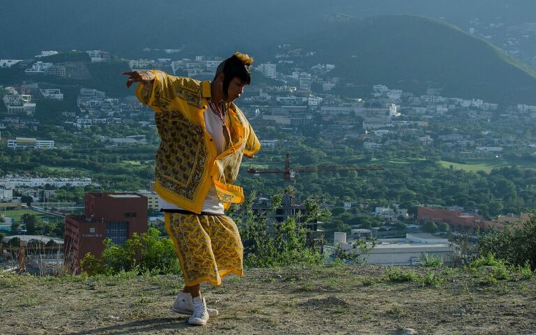 An image of a young man dancing on a hilltop above a city.