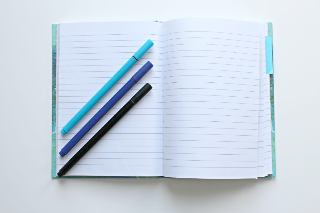 blank notebook with three blue markers improve your English vocabulary by writing things down