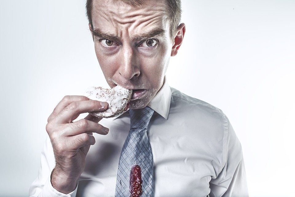 Male professional eating a powdered donut and looking concerned because there is jelly on his tie.