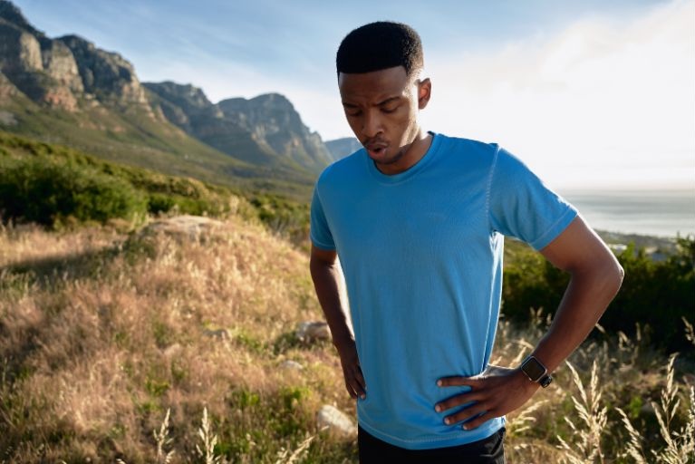 A person in a blue t-shirt standing in front of a mountain catching his breath.