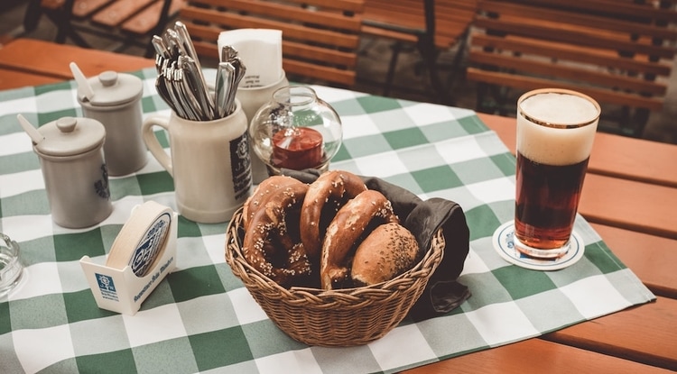 Wooden table with green checked tablecloth with basket of soft pretzels and a glass of beer.