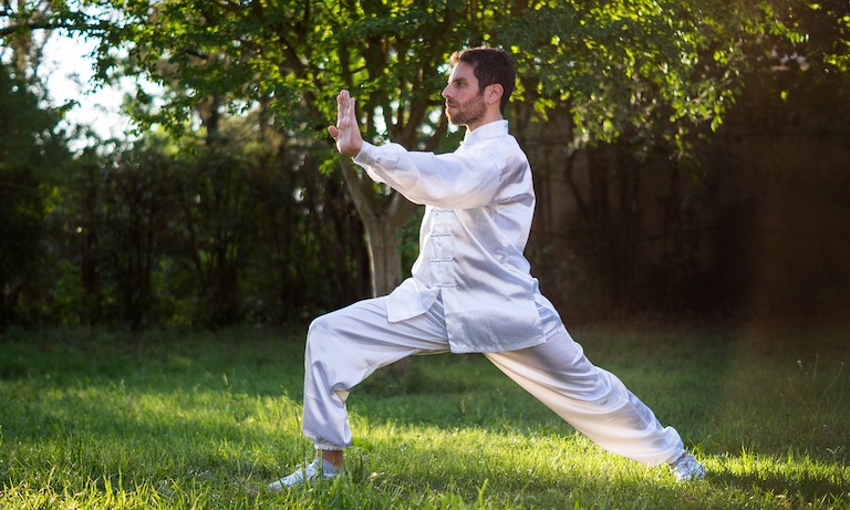 Man wearing a white traditional Chinese outfit and practicing tai chi in a grassy area.