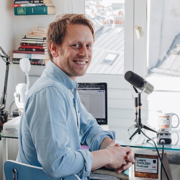 Image of a man sitting at a desk in front of a microphone, smiling at the camera. This is the thumbnail for the Luke's English Podcast. 