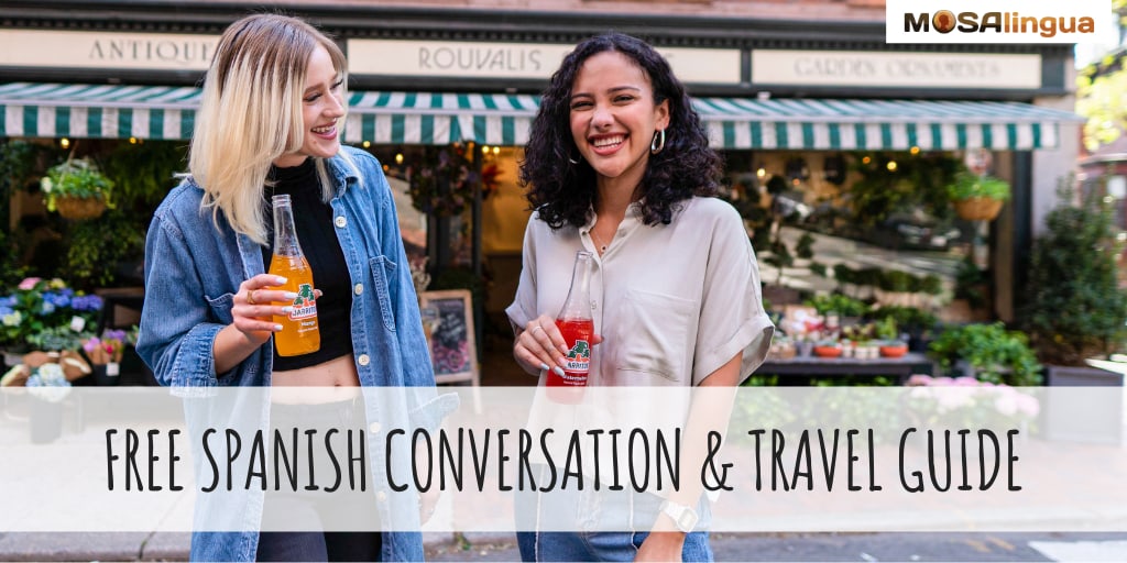 A blonde white woman and a dark-haired Latina woman are standing in front of a garden store, laughing and holding Jarritos sodas. Text reads: Free Spanish Conversation & Travel Guide. MosaLingua.