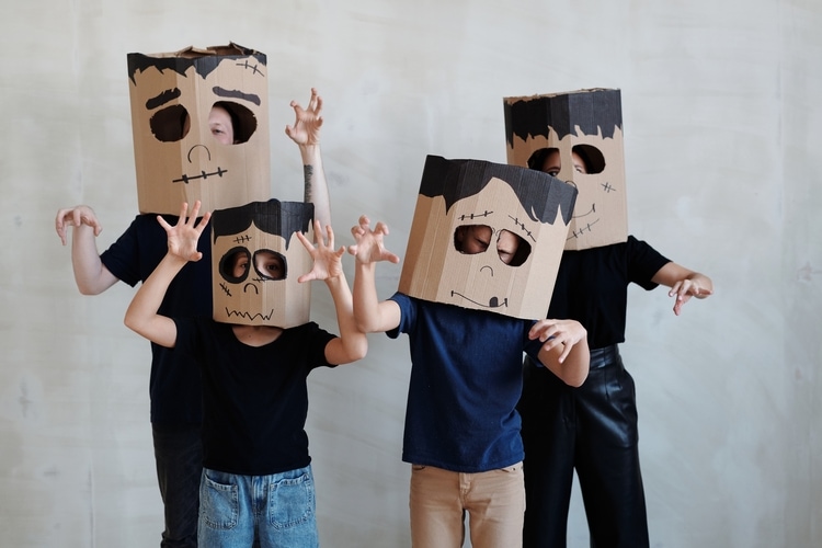 Family of four wearing homemade cardboard Halloween monster masks and putting up their hands as if walking like Frankenstein.