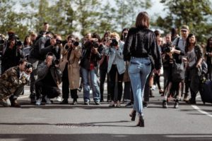 A large group of photographers, or paparazzi, taking pictures of one woman, whose back is to the camera.