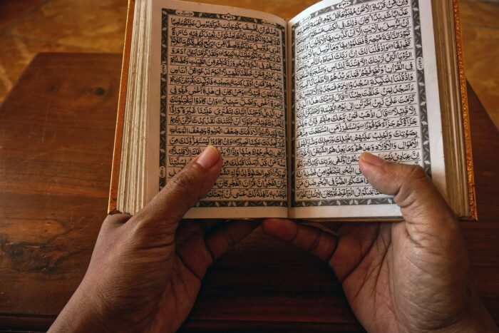 A person's hands holding an open book with Arabic writing inside.