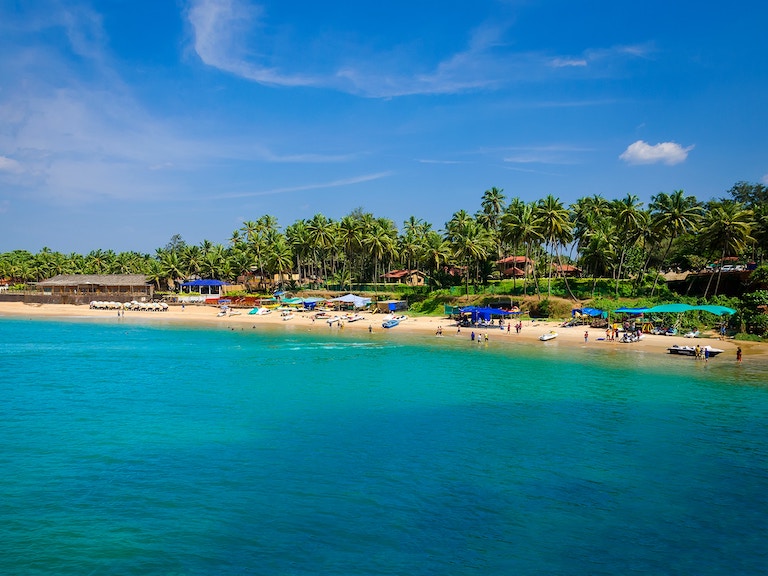 Bright turquoise water and a beach with palm trees in Goa, India.